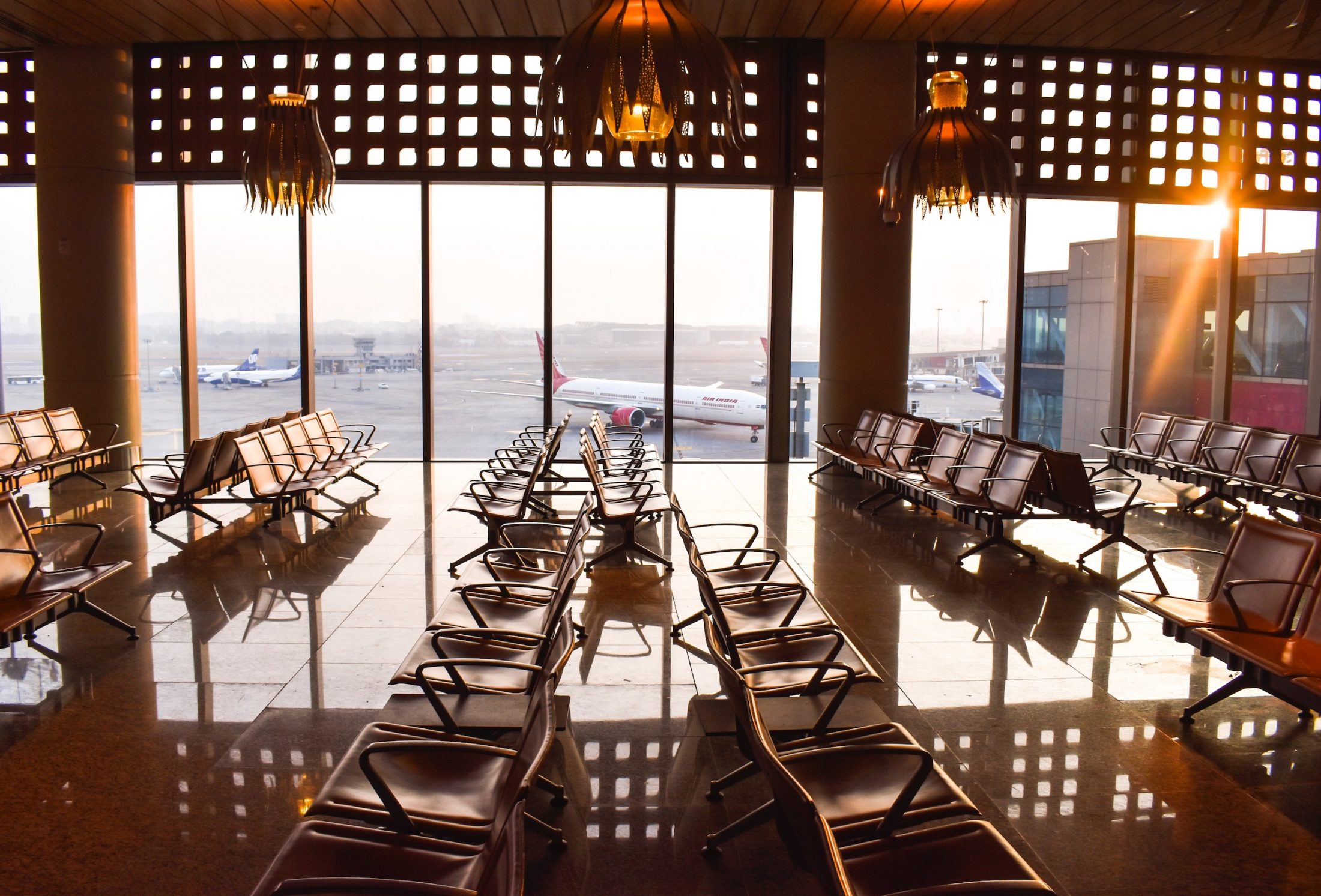 coping-with-long-layovers-header An airport waiting area with decorative lighting and large windows looking over planes