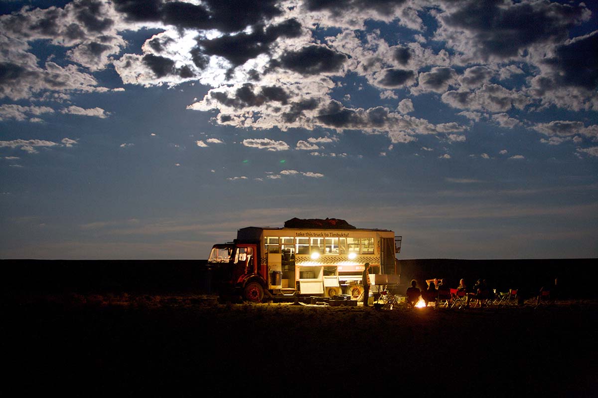 A group sits around a campfire beside and overlanding truck at night