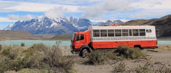 Dragoman Overland truck parked besides a lake with mountains in the background