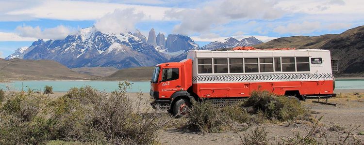 Dragoman Overland truck parked besides a lake with mountains in the background
