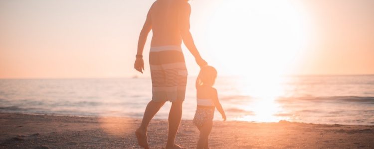 Parent and child walking on a beach at sunset