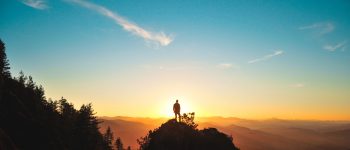 Person standing on top of rocks looking at the sunset