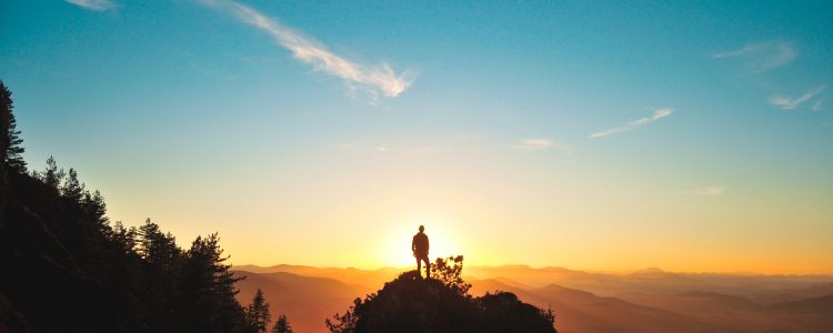 Person standing on top of rocks looking at the sunset