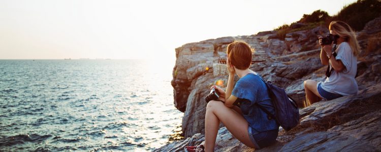 Two women sitting on rocks by the sea at dusk