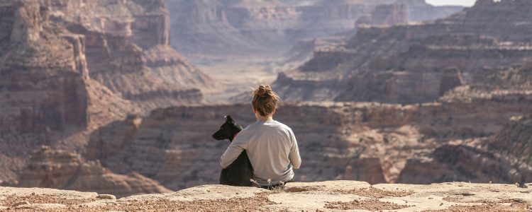 Woman sitting with dog aove a canyon
