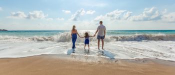 Man, woman and child hold hands standing in the surf on a beach