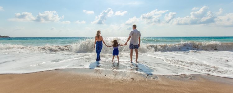 Man, woman and child hold hands standing in the surf on a beach