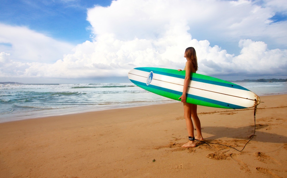 Girl with a surf board on a beach in Sri Lanka